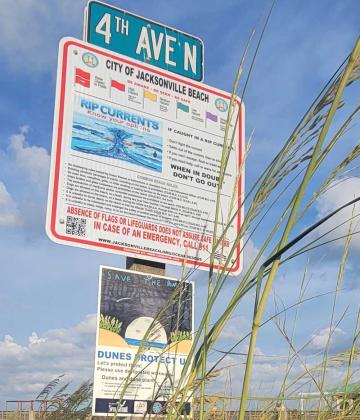 A sign posted beneath a rip current warning in Jacksonville Beach urges beachgoers to "Save the Dunes."